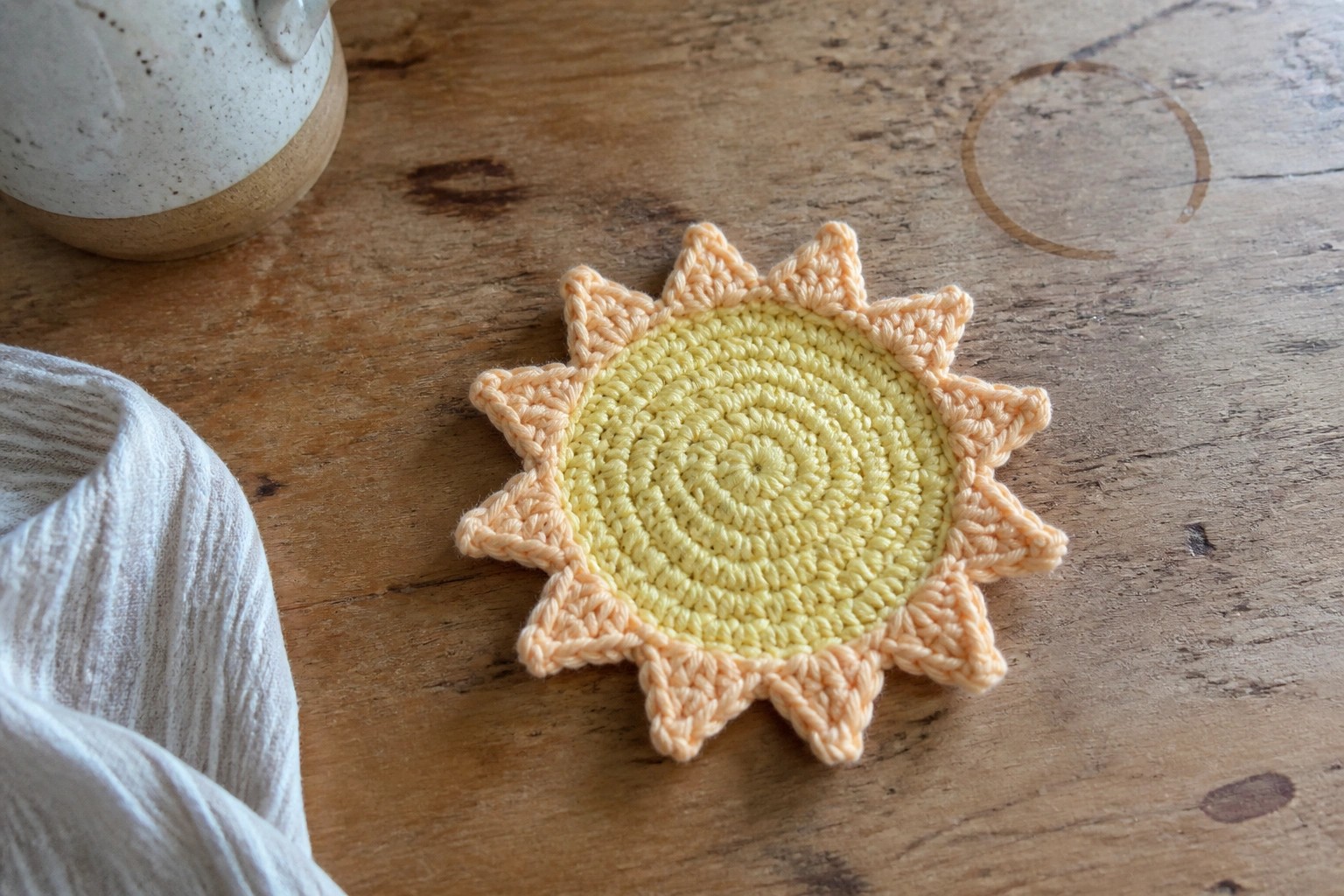 A crocheted sun-shaped coaster in yellow and peach rests on a wooden table.