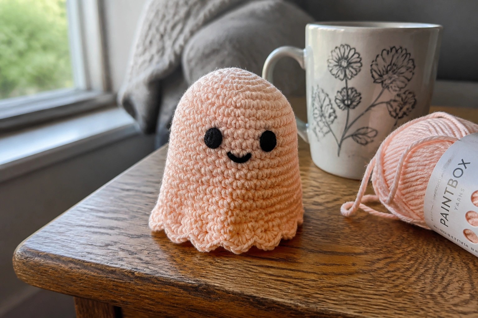 Pink crocheted octopus toy on wooden table beside mug and yarn skein