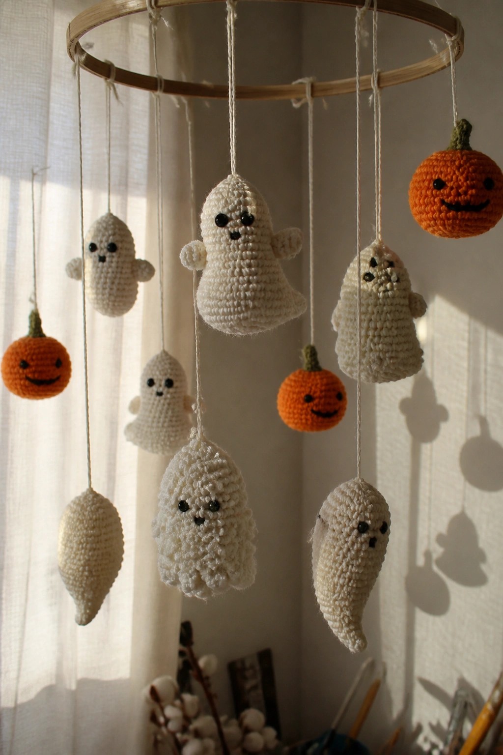 Crocheted white ghosts and orange pumpkins hanging from wooden hoop mobile.