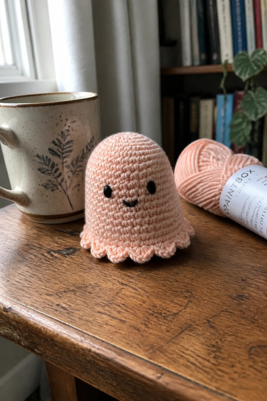 Pink crocheted octopus toy on wooden table beside mug and yarn skein