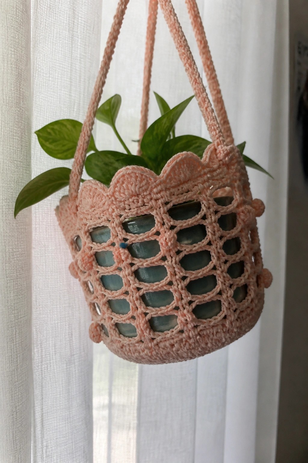 Peach crocheted hanging basket with openwork pattern and green plant in blue pot