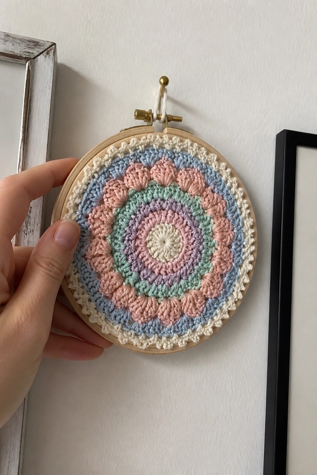 Hand holds embroidery hoop with pastel crocheted mandala on white wall