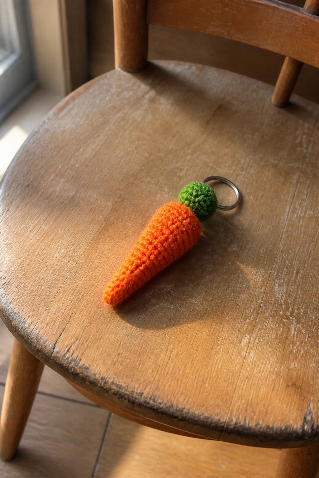Fuzzy orange crocheted carrot keychain with green top on wooden chair