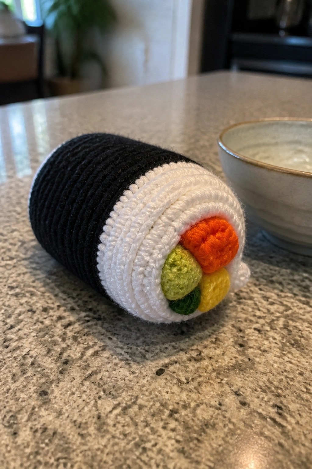 Crocheted sushi roll with black nori, white rice, and colorful fillings on countertop