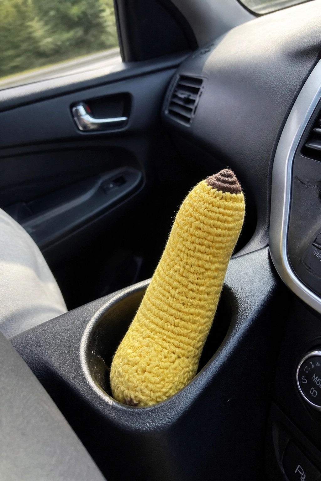 Yellow crocheted banana with brown tip in car cup holder