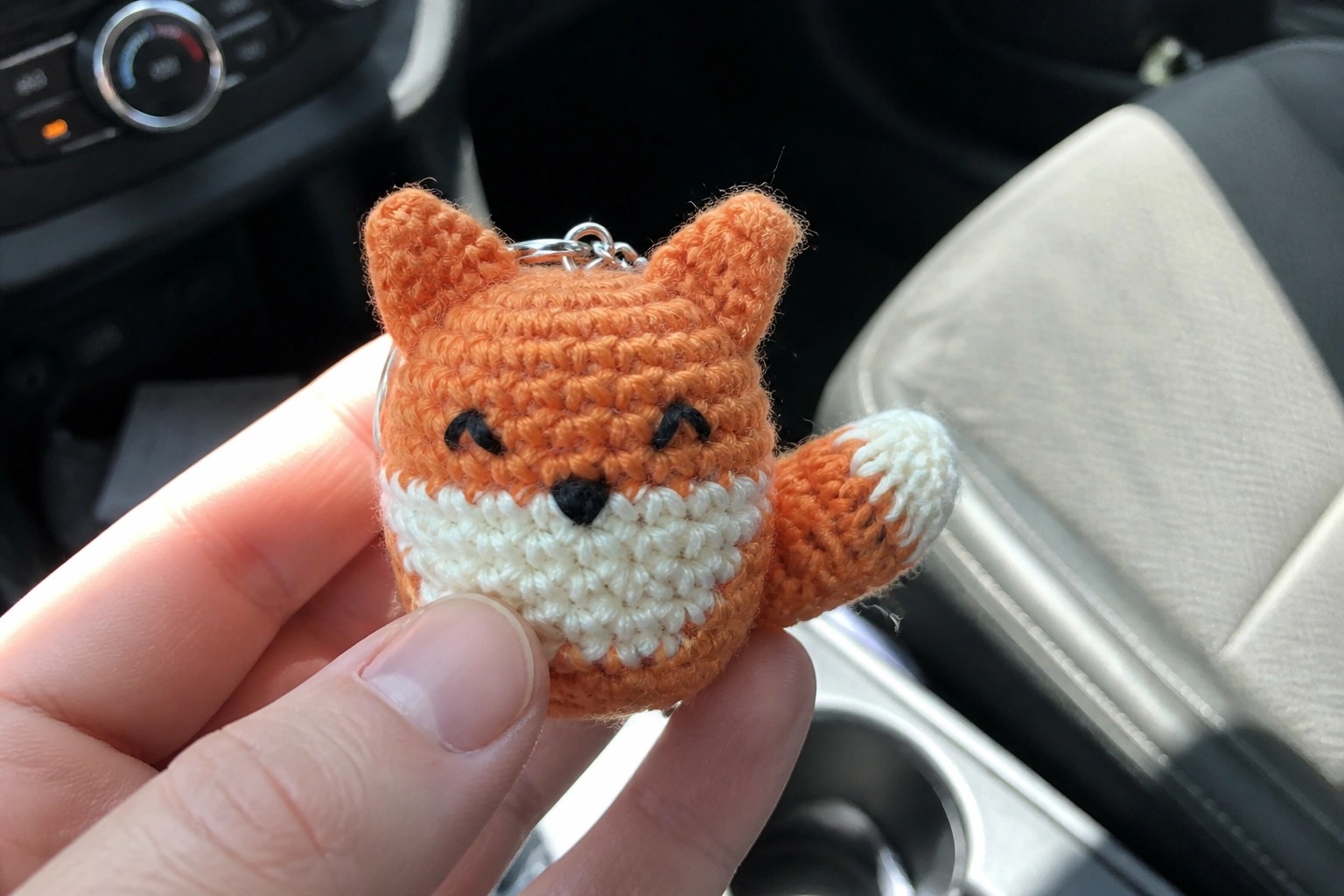 Hand holding small orange crocheted fox keychain with white accents in car