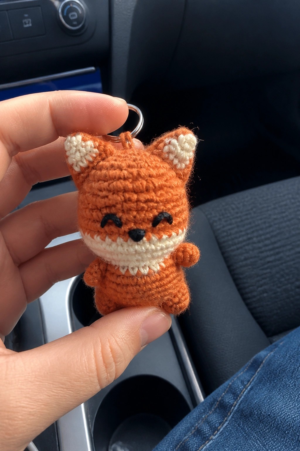 Hand holding small orange crocheted fox keychain with white accents in car