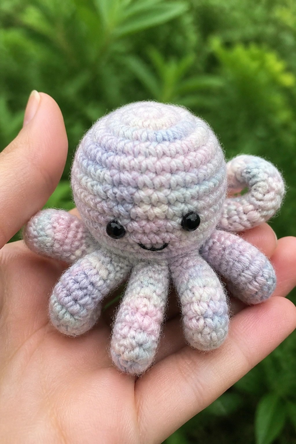 Tiny pastel crocheted octopus toy with black eyes held in an open hand