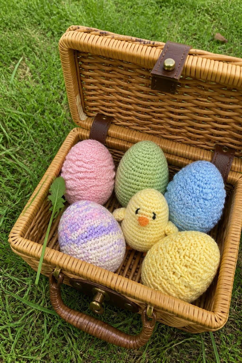 Open wicker basket on grass holding pastel crocheted eggs and yellow chick.