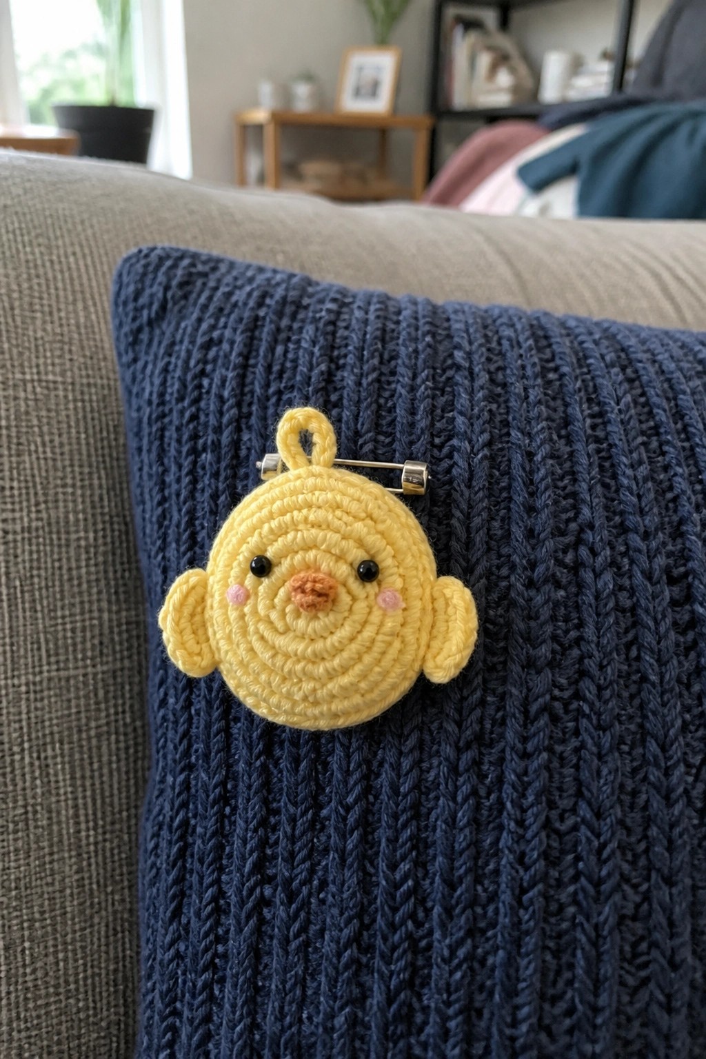 Yellow crocheted chick brooch pinned to dark blue ribbed knit pillow.