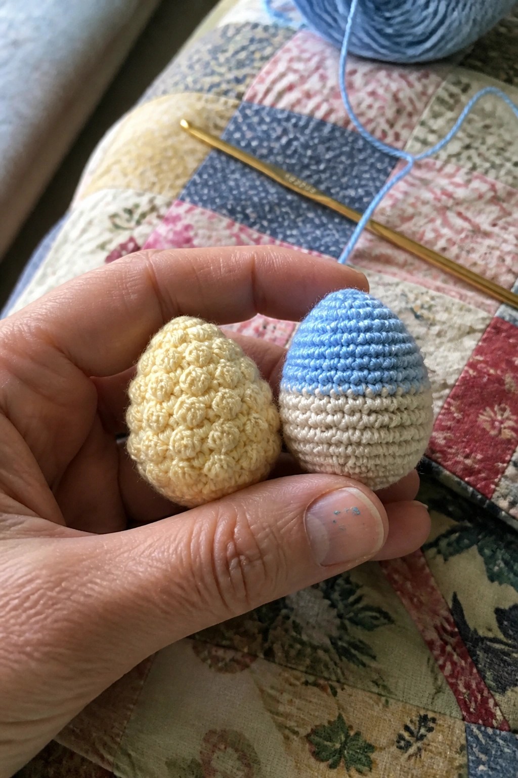 Hand holding yellow and blue crocheted eggs near gold hook on quilt