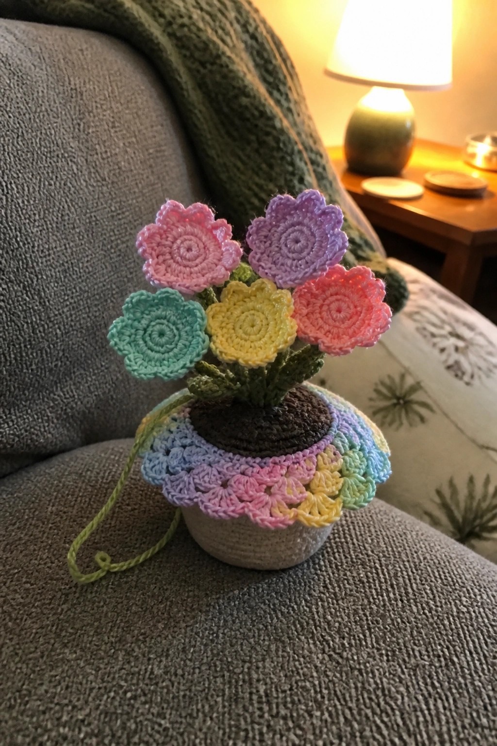 Colorful crocheted flowers in a rainbow pot on a gray couch