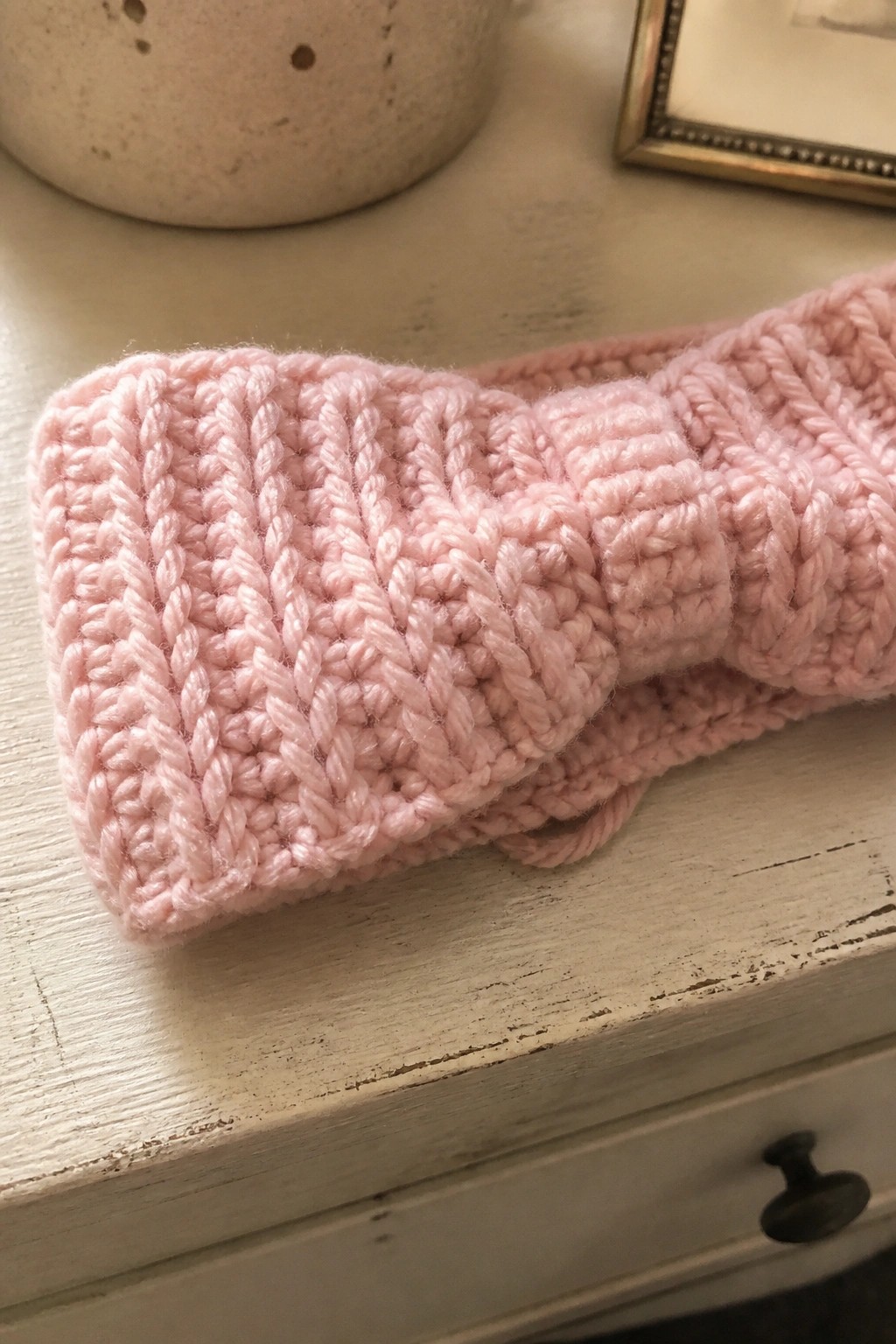 Pink knitted headband with bow on distressed white wooden surface