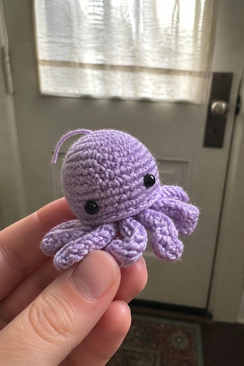 Hand holding a small purple crocheted octopus with black eyes