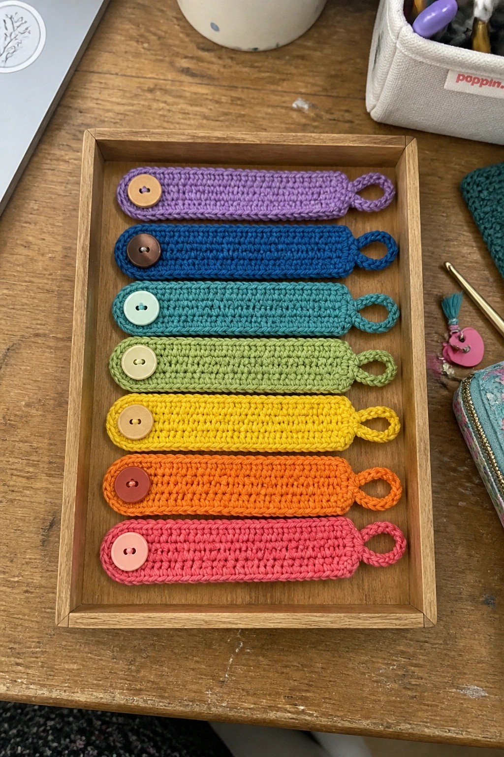 Rainbow crocheted strips with buttons lined in a wooden tray