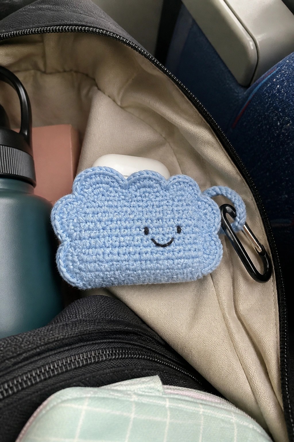 Blue crocheted cloud with smiling face on carabiner inside open gray bag