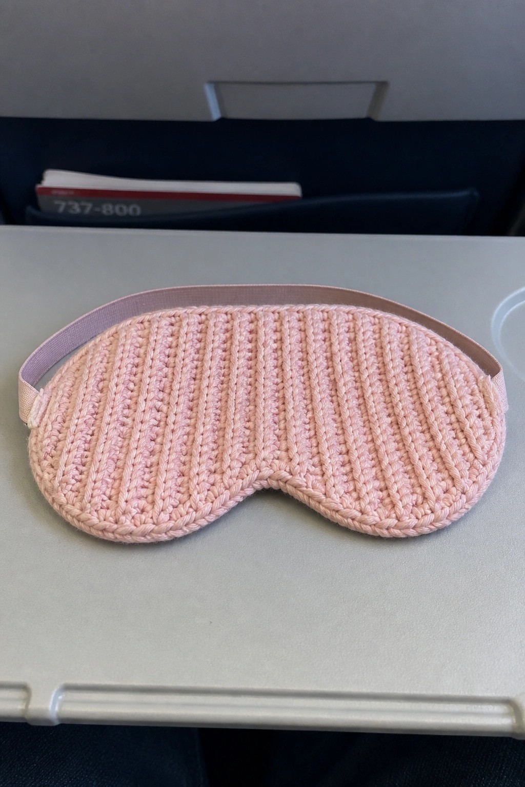Pink knitted sleep mask with elastic strap on airplane tray table