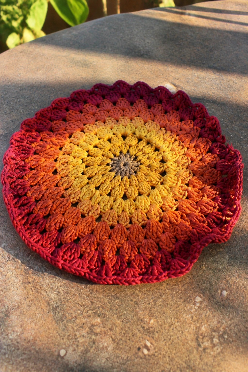 Crocheted circular doily in yellow-to-red gradient on sunlit stone surface