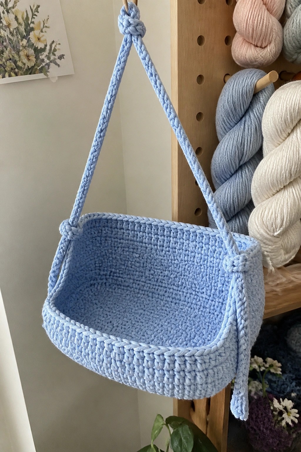 Light blue crocheted shoulder bag hanging from wooden peg near yarn skeins.