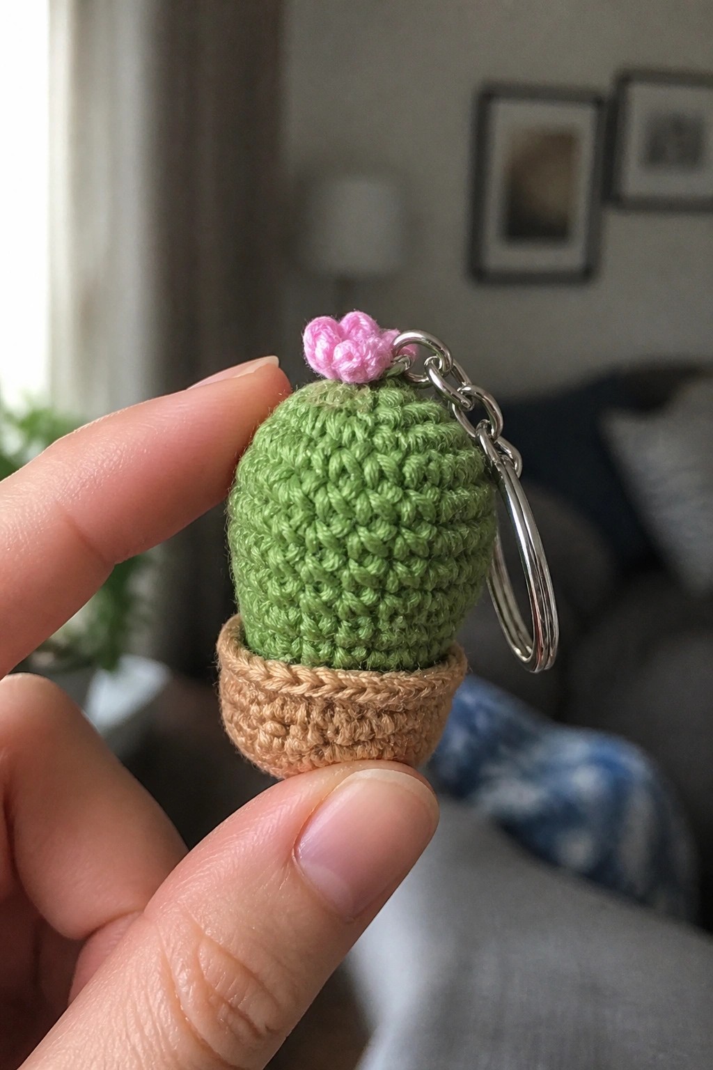 Hand holding crocheted green cactus keychain with pink flower in brown pot and metal ring