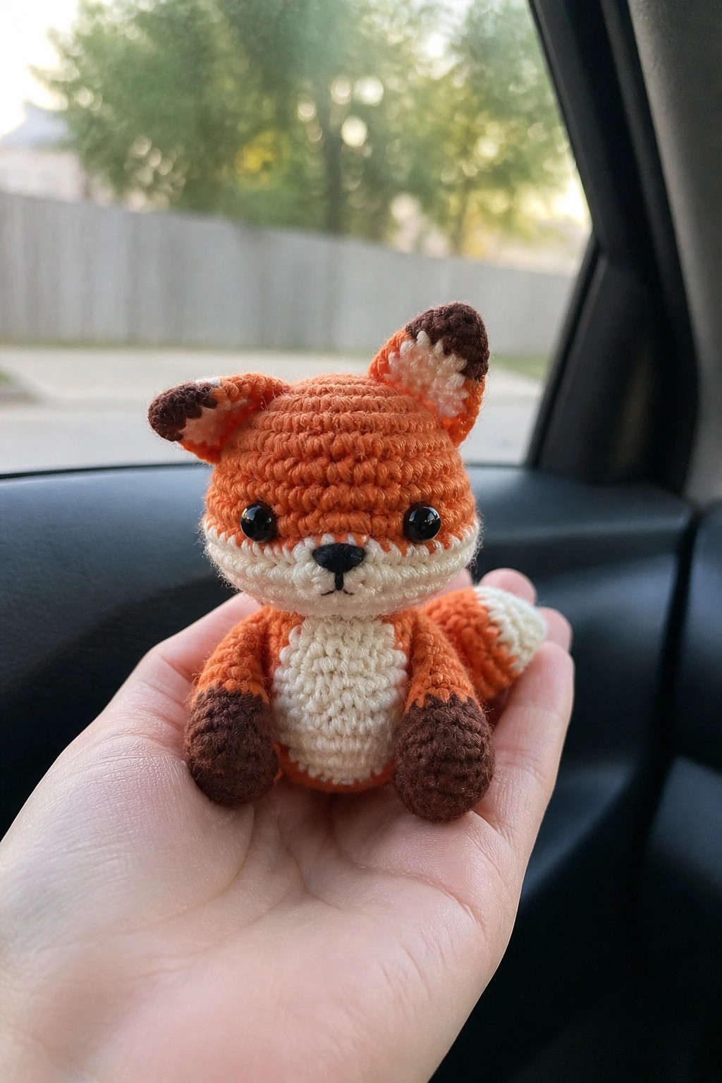 Hand holding small crocheted orange fox with white belly and brown accents in car