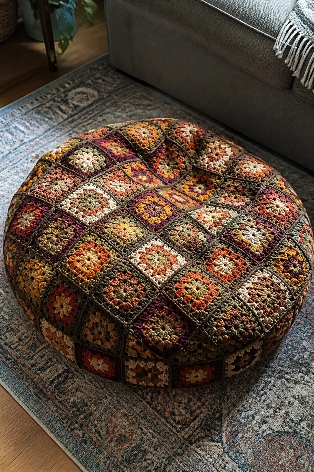 Colorful crocheted pouf of granny squares on patterned rug by gray sofa