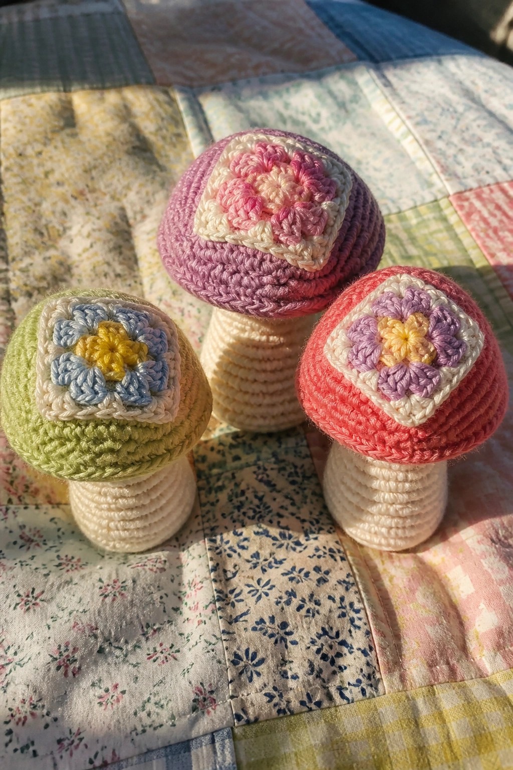 Three crocheted mushrooms with floral granny square tops on a patchwork quilt.