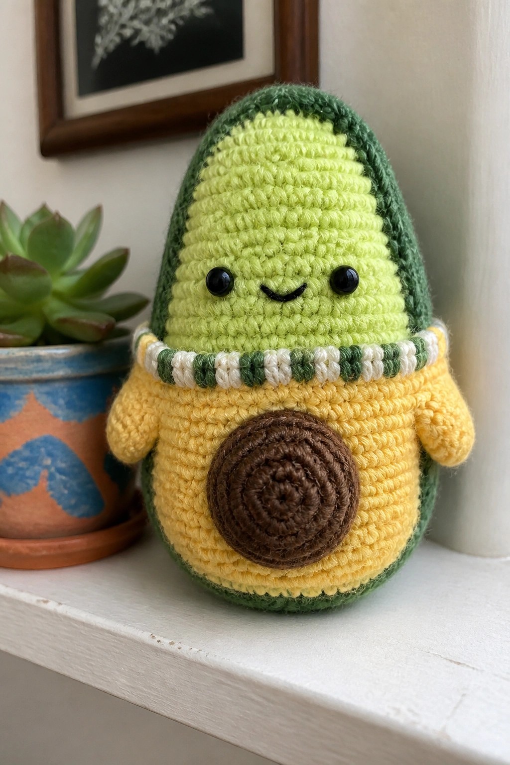 Crocheted avocado plush with smiling face, yellow arms, brown pit on white shelf