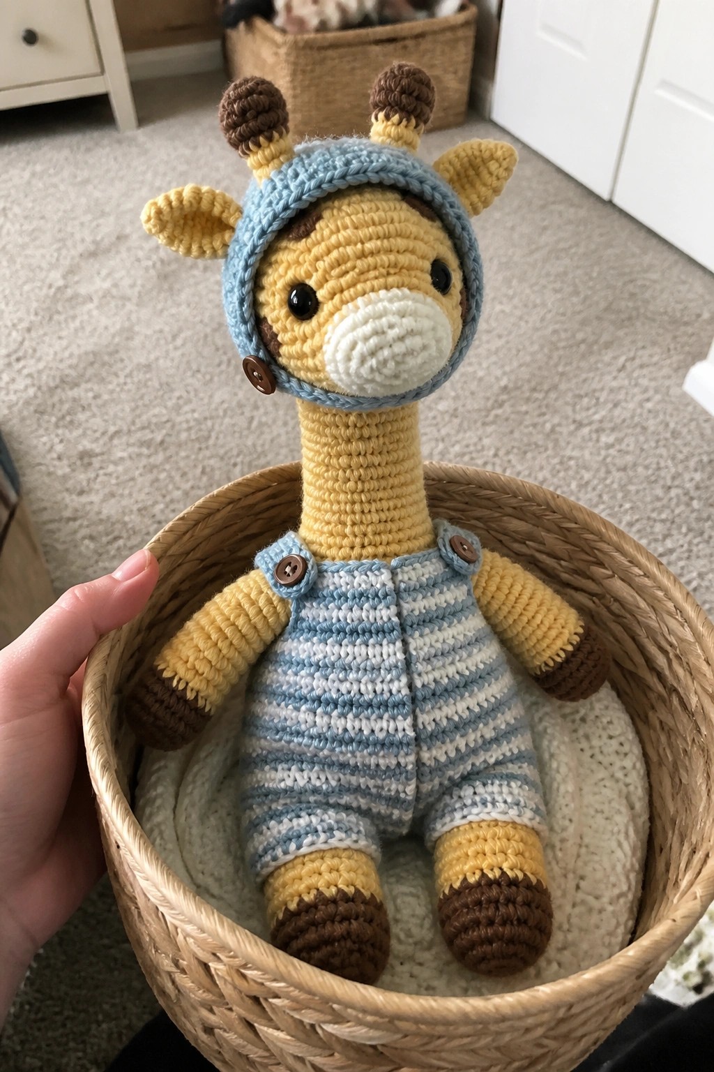 Crocheted yellow giraffe in blue hat and striped overalls inside woven basket