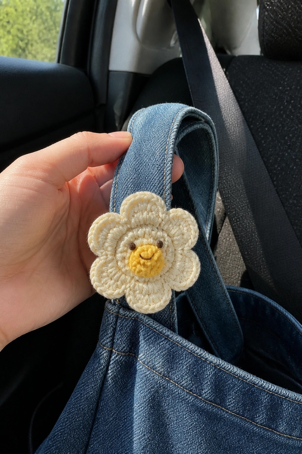 Hand holding blue denim bag with smiling crocheted daisy flower pin