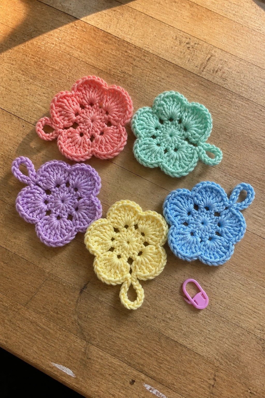Five pastel crocheted flower motifs on wood with a pink clip.