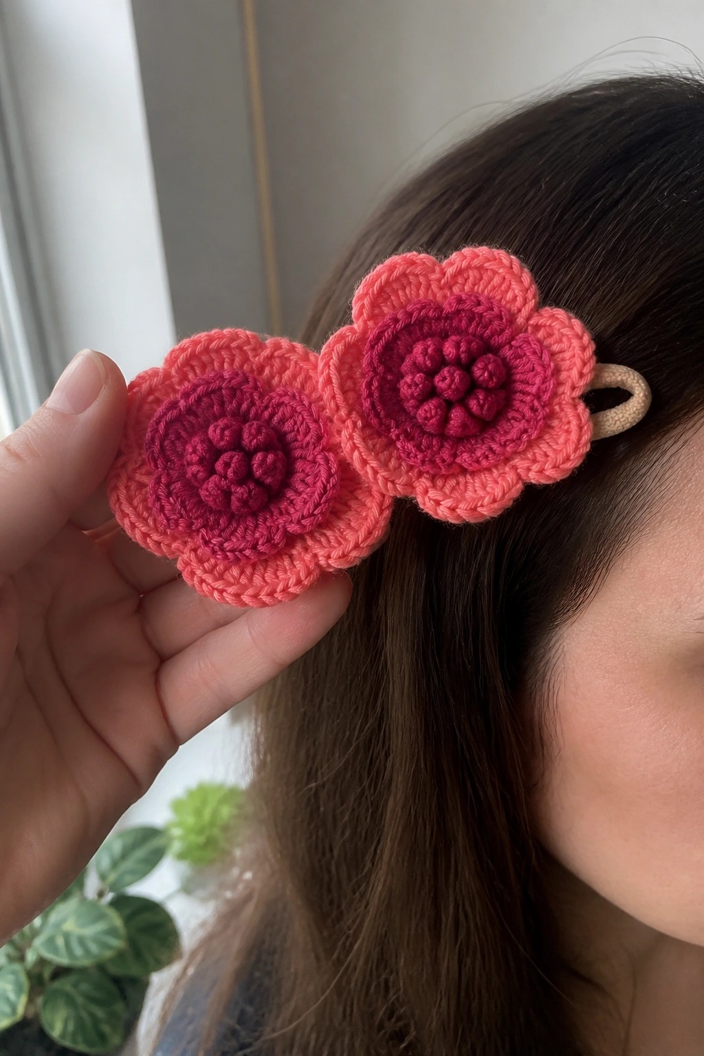 Hand holding two pink crocheted flower hair clips near dark brown hair.
