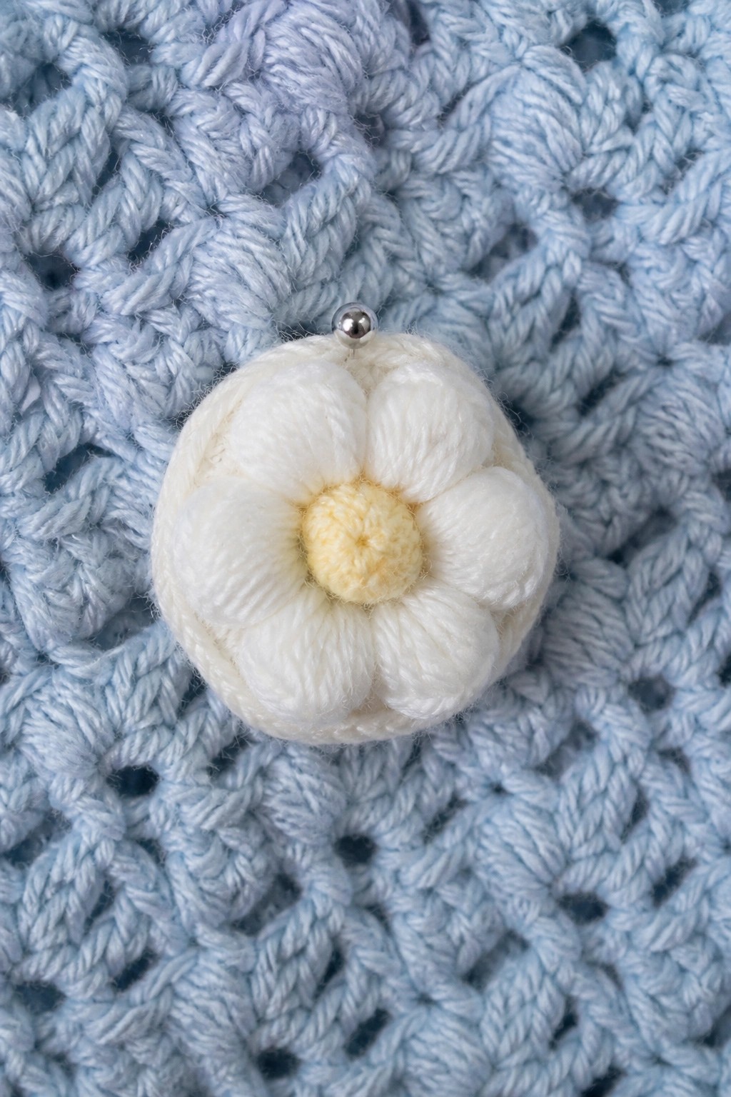 White crocheted flower with yellow center pinned on light blue fabric