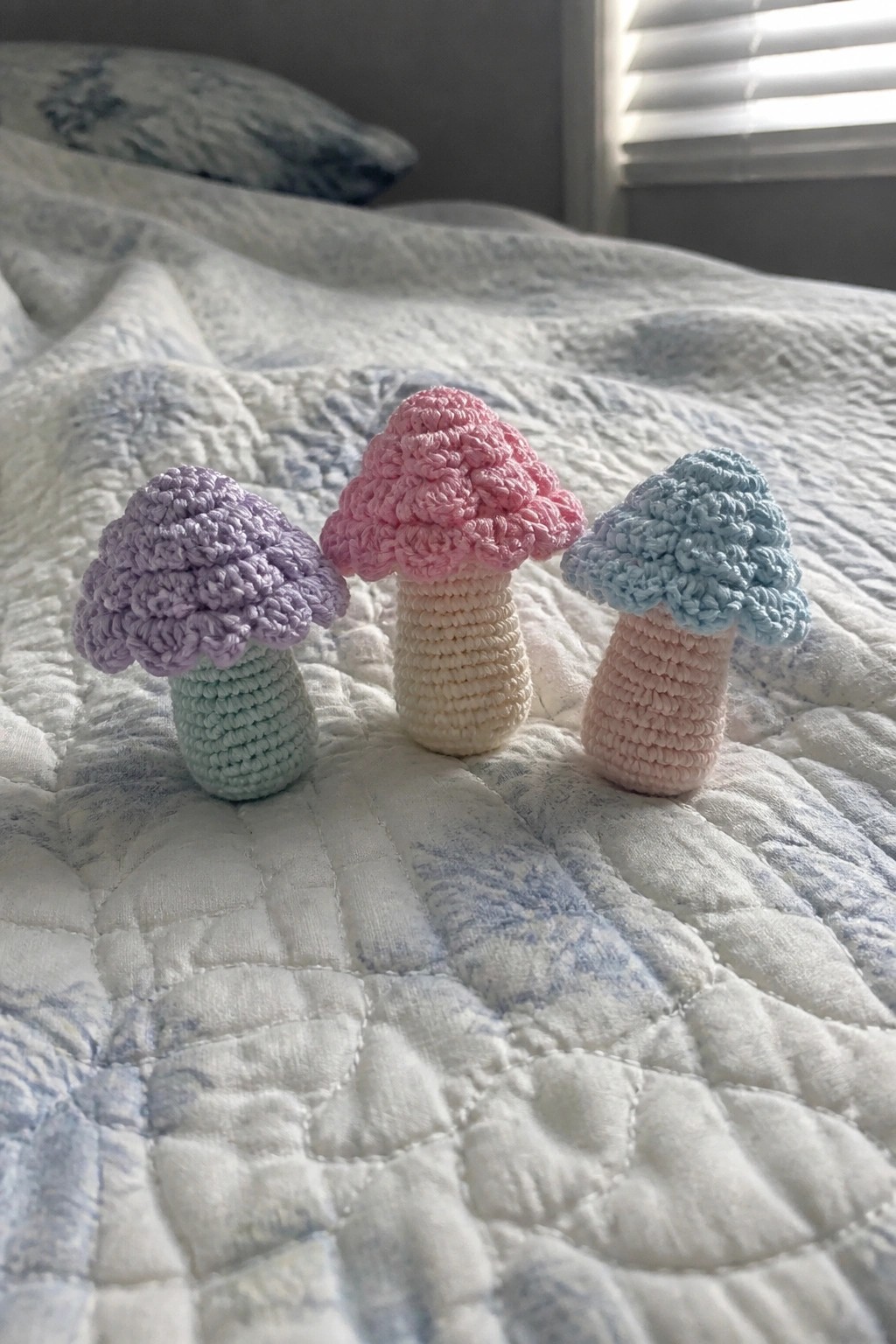Three pastel crocheted mushrooms on a white quilted bedspread