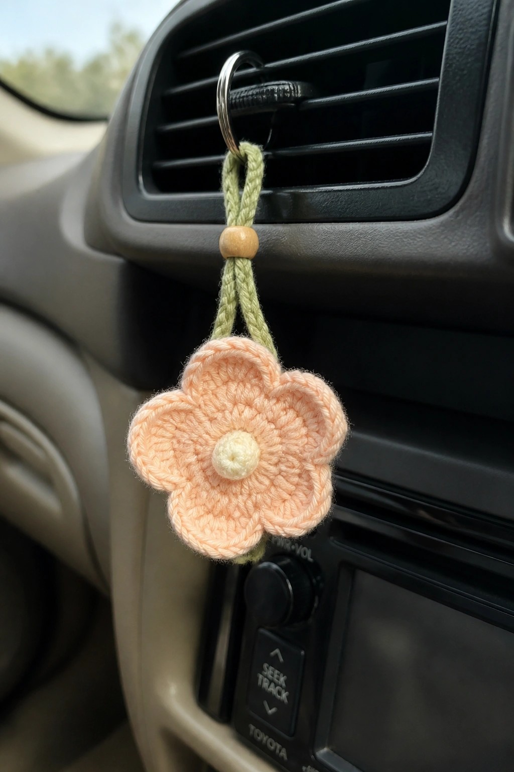 Crocheted peach flower on green cord hanging from car air vent