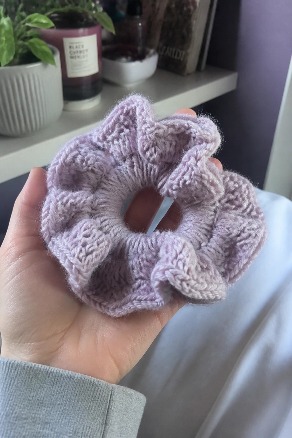 Hand holding fluffy lavender knitted scrunchie with gray sleeve visible