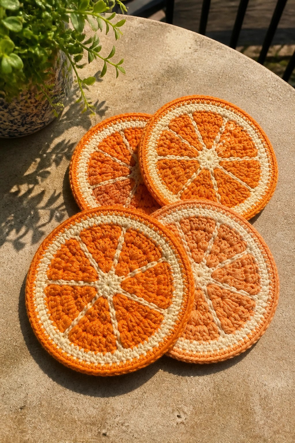 Four crocheted orange slice coasters on a stone table with potted plant