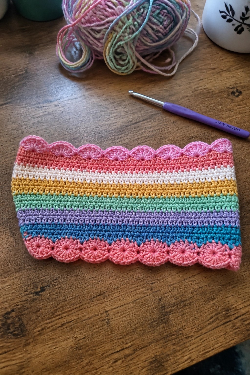 Rainbow crocheted swatch with pink scalloped edges beside hook and yarn on wood