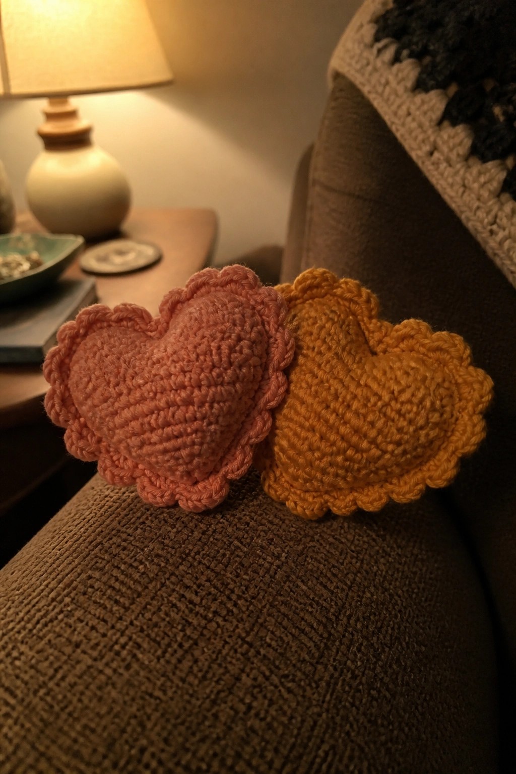 Pink and yellow crocheted hearts resting on brown textured couch arm