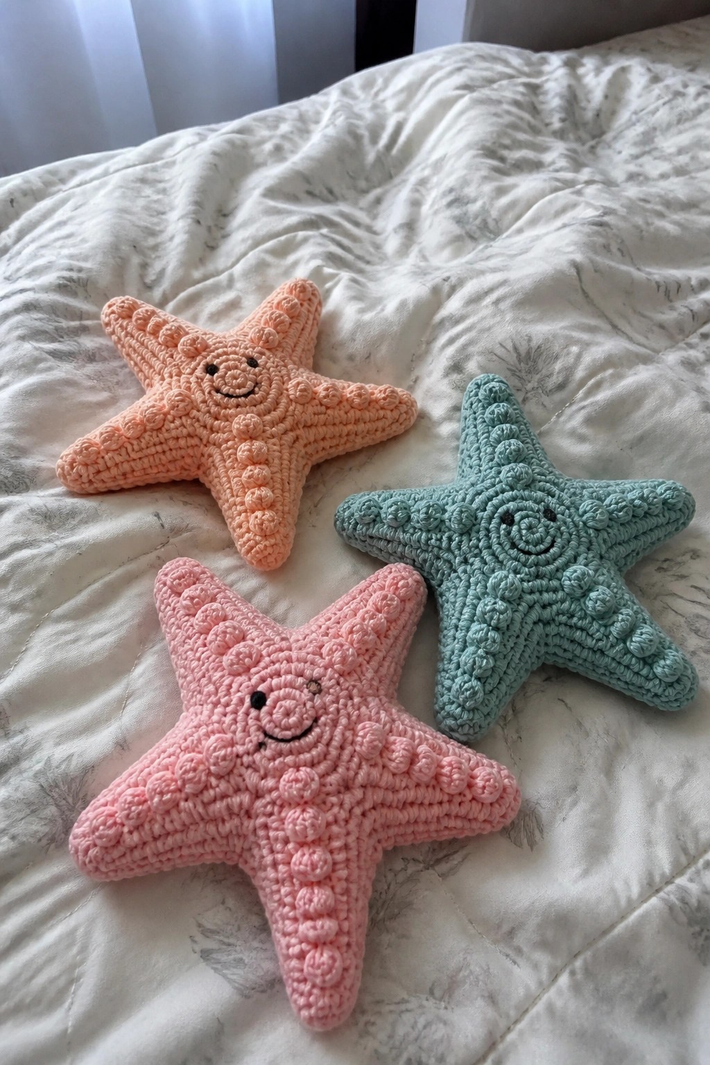 Three crocheted starfish plush toys with smiling faces on white bedding