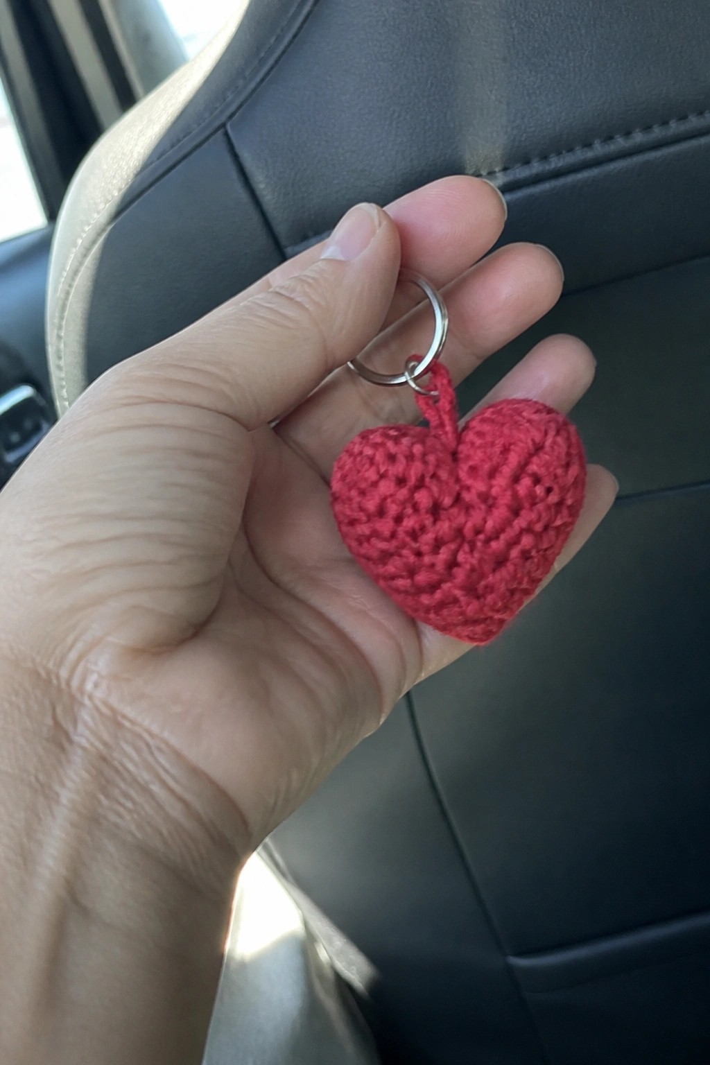Hand holding red crocheted heart keychain with silver ring inside car