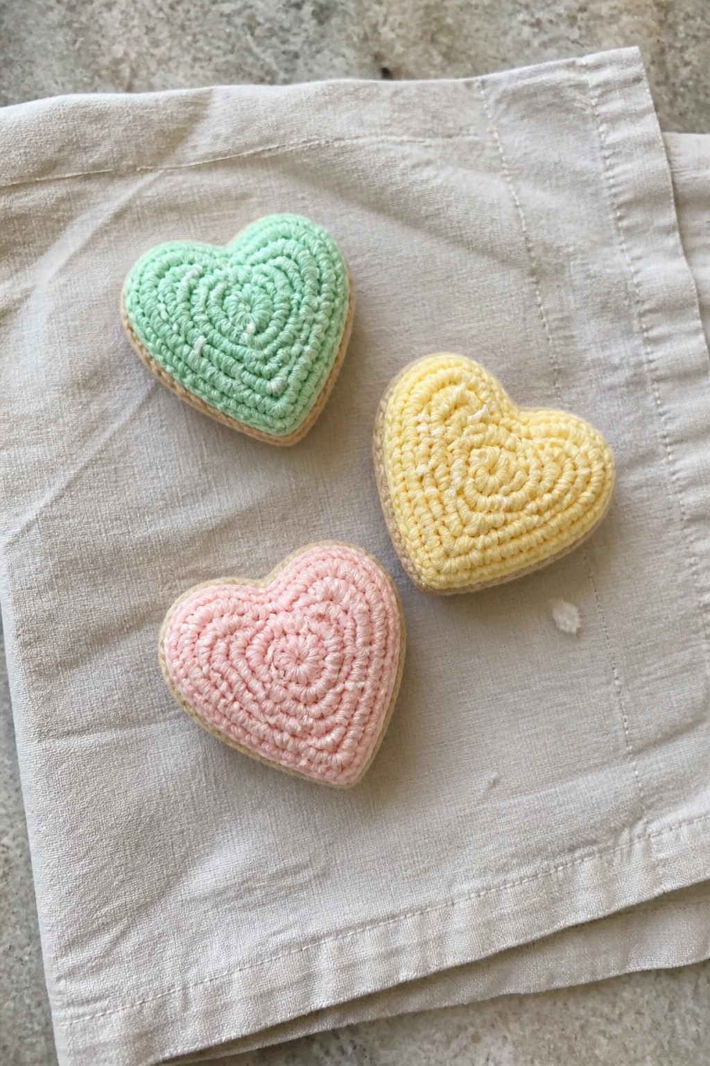 Three pastel heart-shaped cookies with spiral icing on white cloth