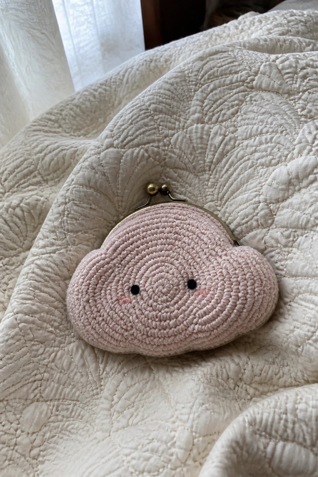 Pink crocheted cloud coin purse with face on white quilted blanket
