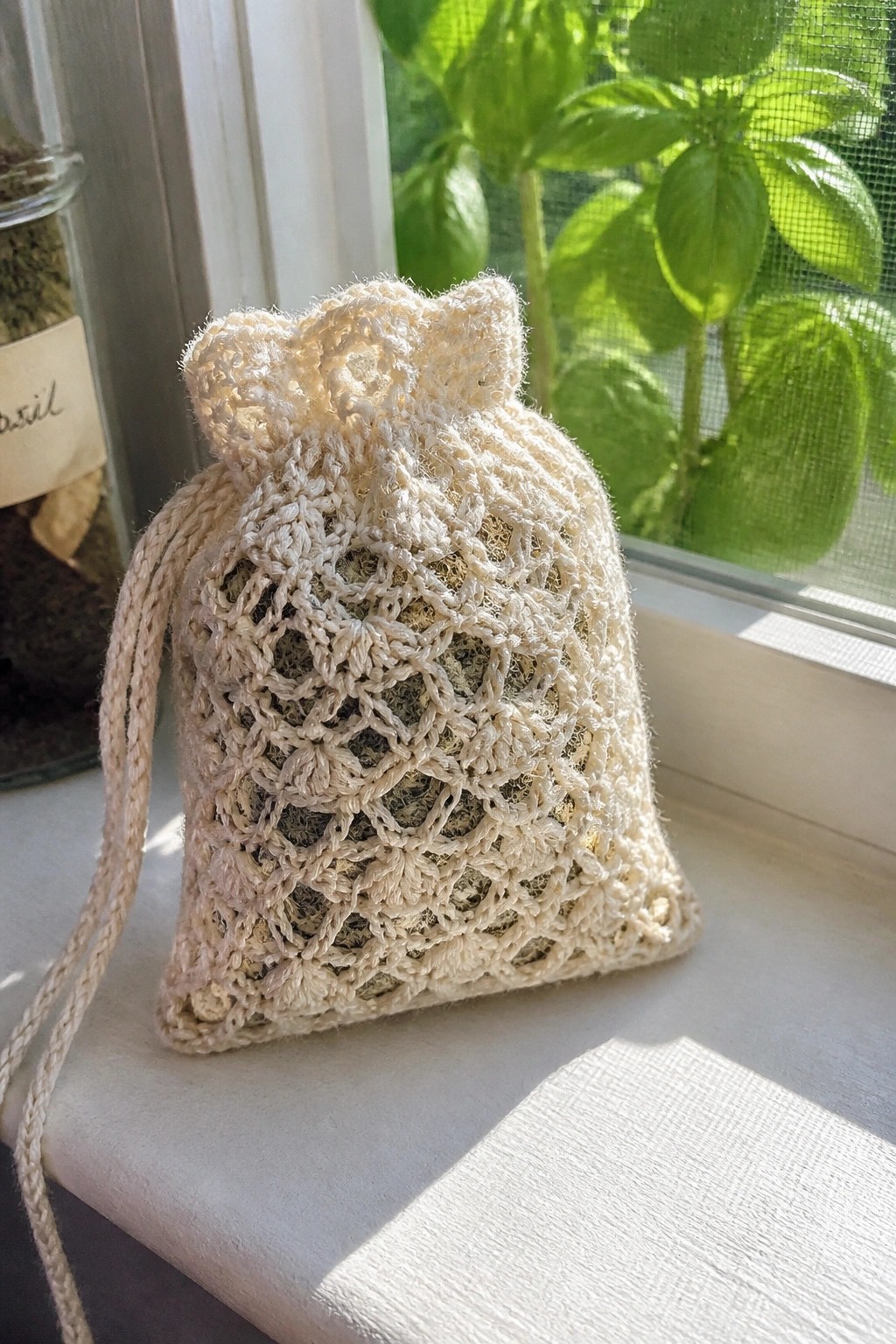 Cream crocheted lace drawstring bag with dried herbs on sunny windowsill