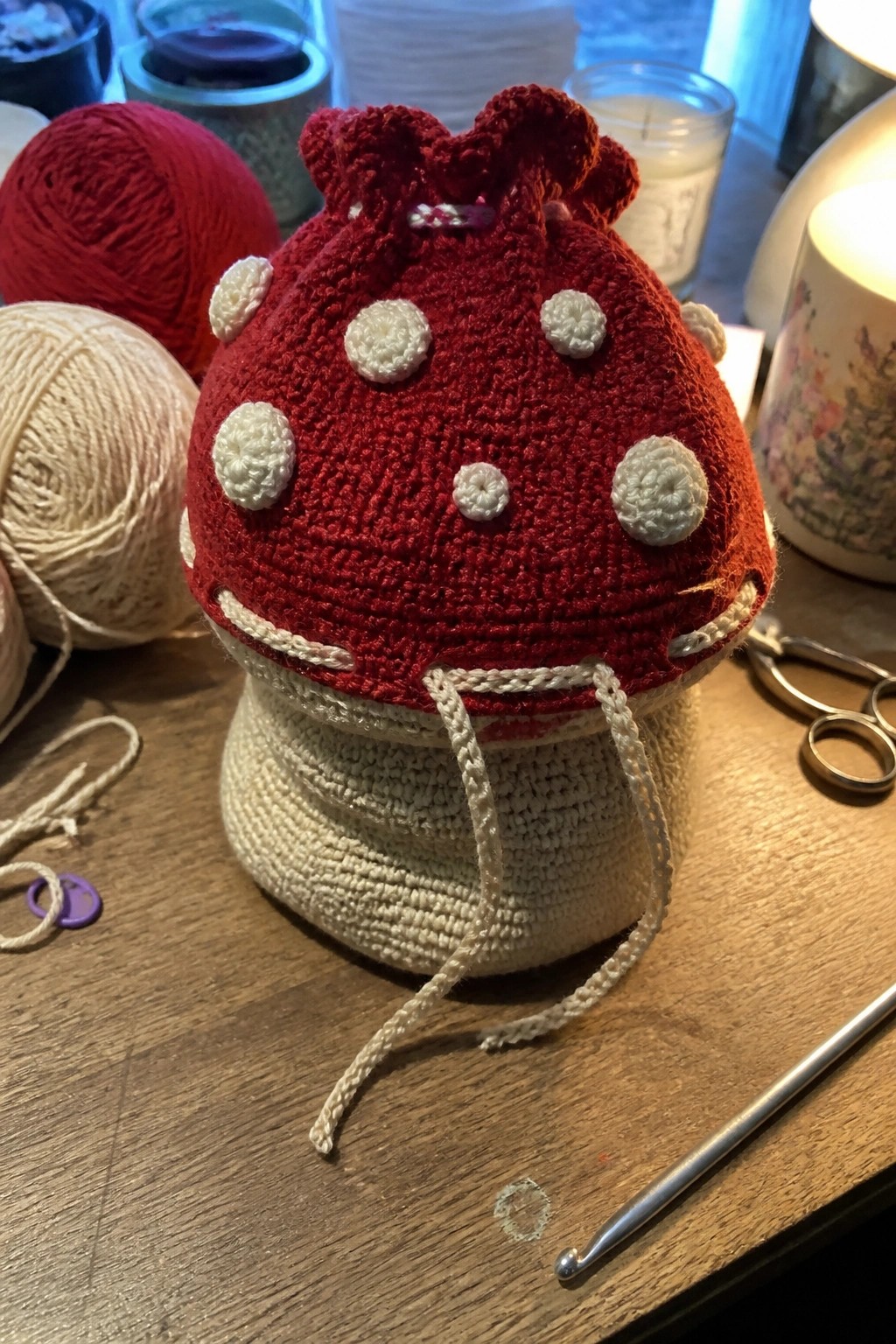 Crocheted red mushroom pouch with white dots and drawstrings on wooden table