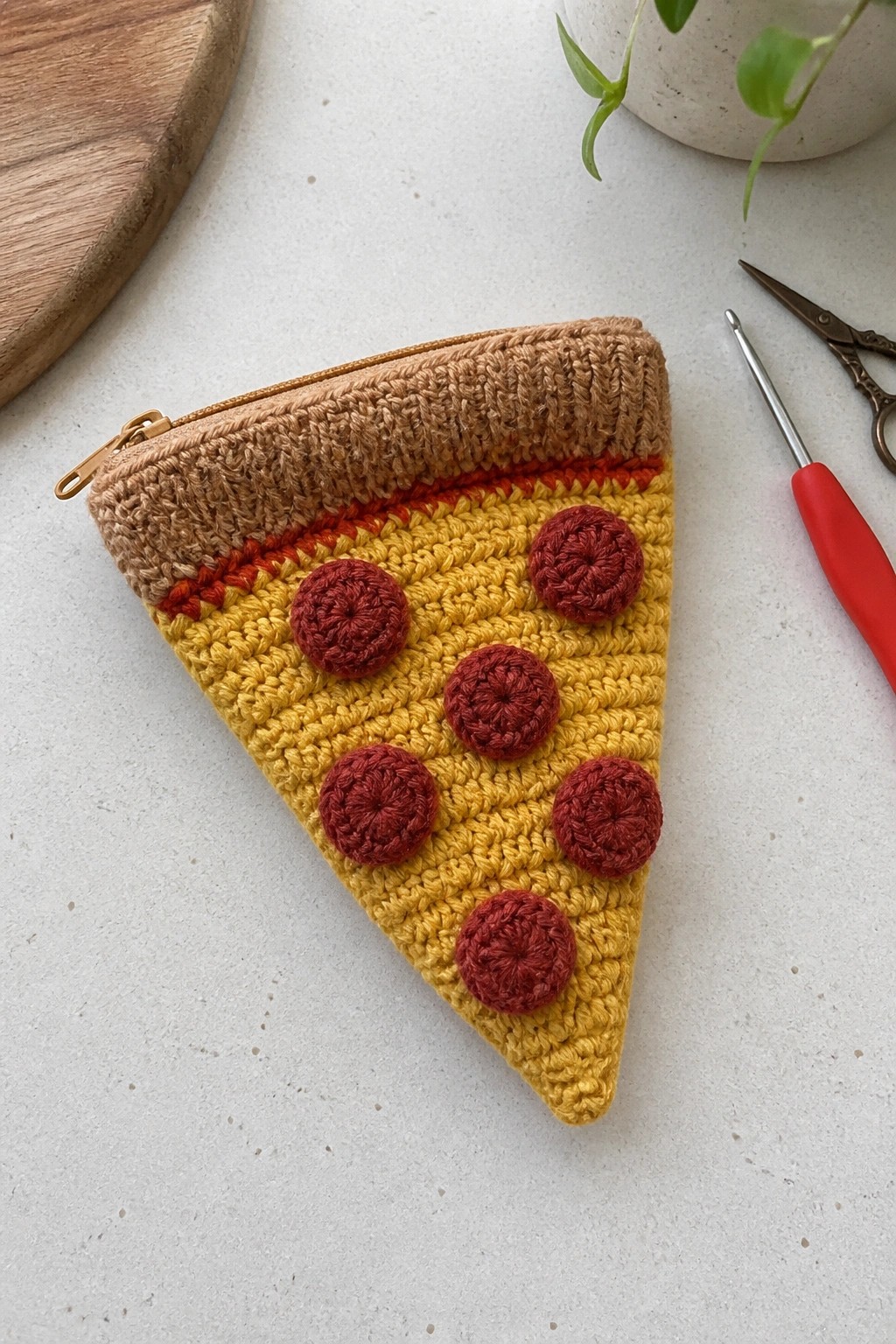 Crocheted yellow pizza slice pouch with red toppings, brown crust, and gold zipper