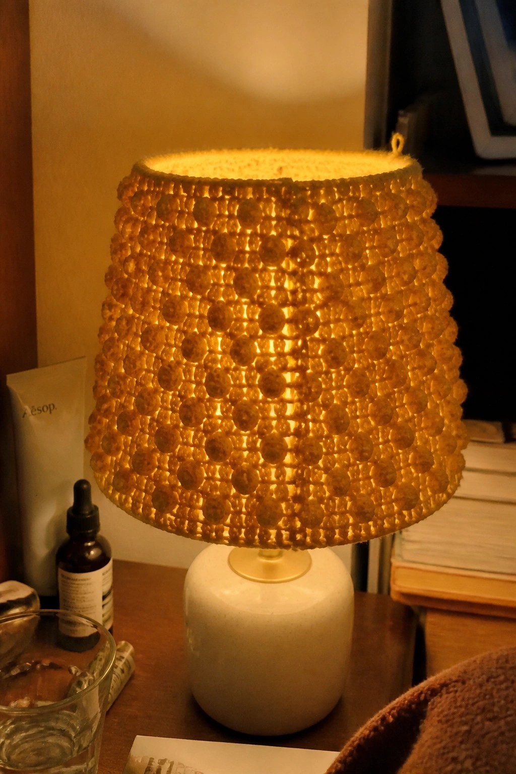 Glowing beaded yellow lampshade on white ceramic base atop wooden table.