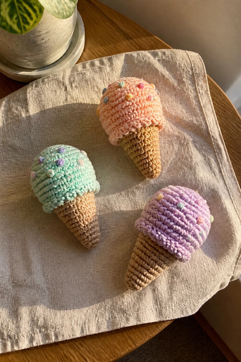 Three crocheted ice cream cones in peach, mint, and lavender on beige cloth