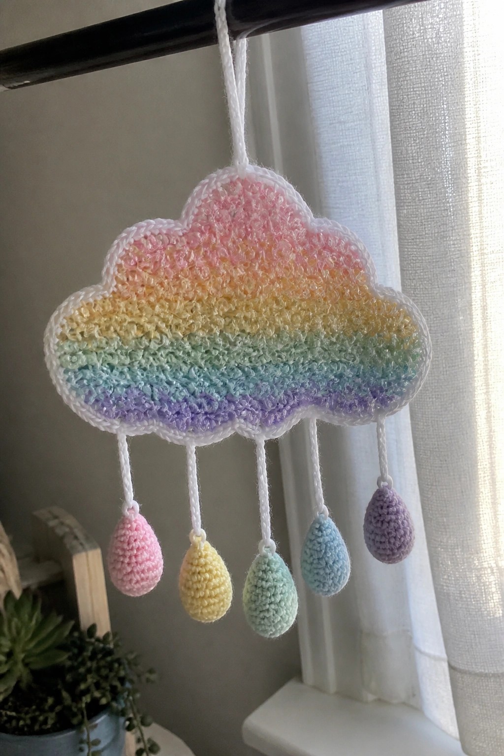 Crocheted rainbow cloud with white border and five dangling pastel raindrops.