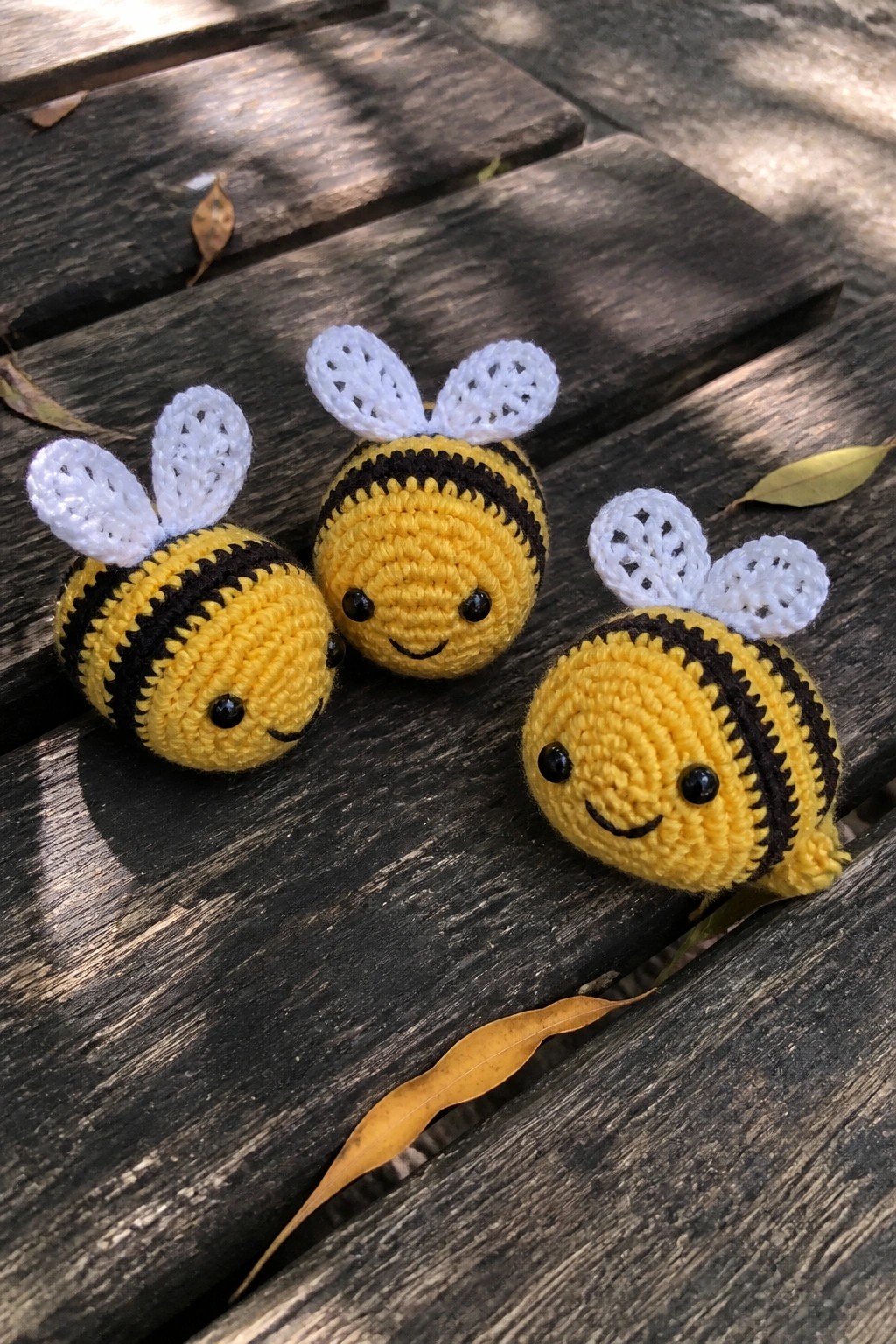 Three yellow crocheted bees with black stripes and white wings on wooden planks